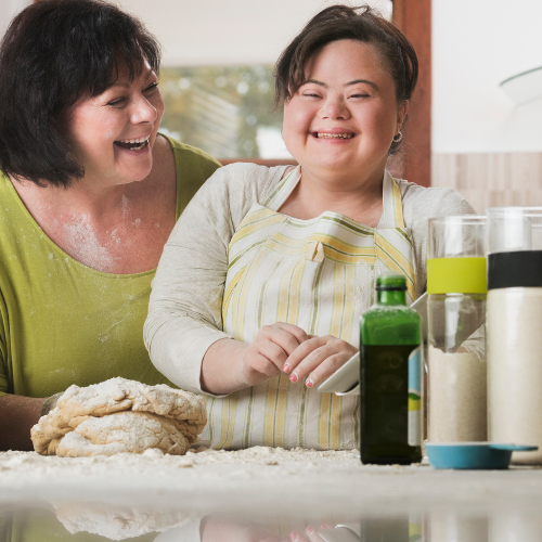 Two women laughing in a kitchen preparing food.